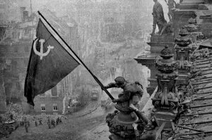 A black and white photo depicting Soviet soldier Abdulkhakim Ismailov, raising the flag of the Soviet Union over the Reichstag in Berlin