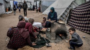 Palestinian civilians in Rafah huddle around a campfire